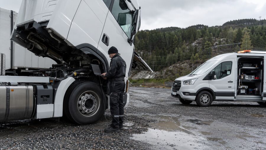 Teknikar med laptop ved ein lastebil med opna førarhus og servicebil i bakgrunnen